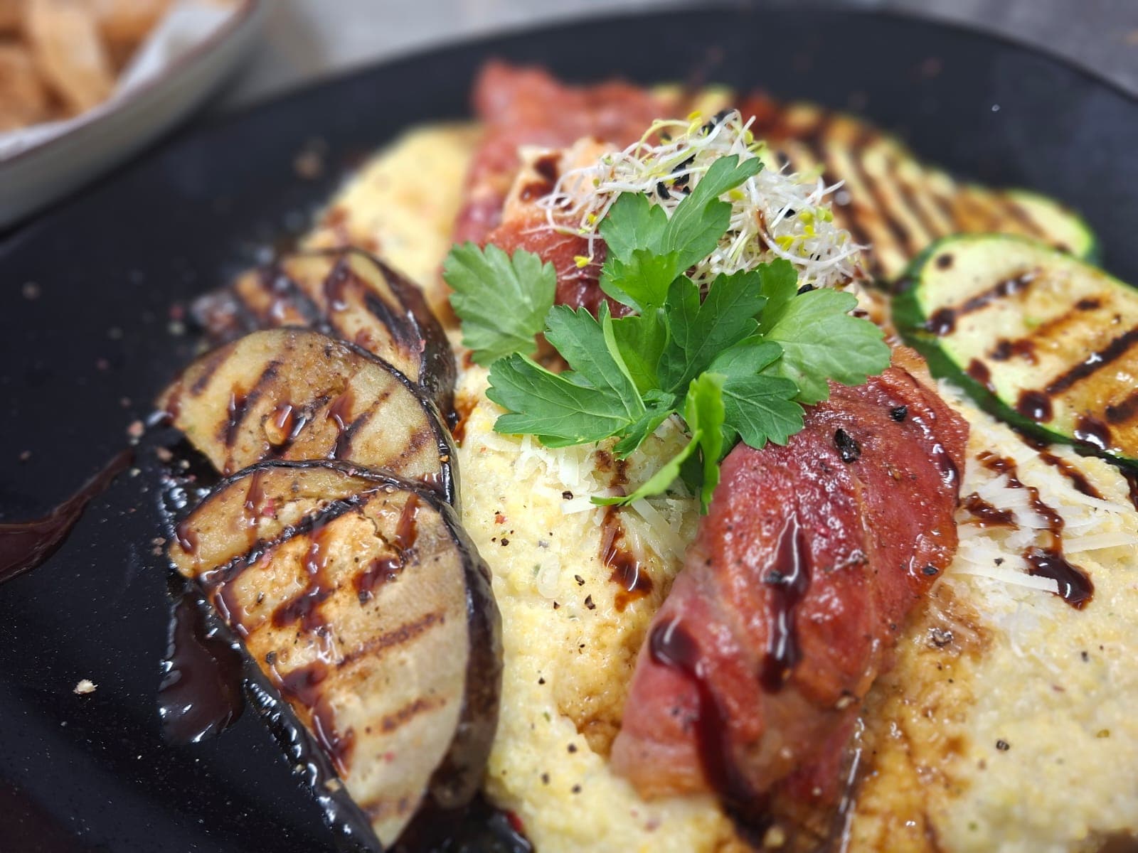 Mediterranes Gericht mit Polenta und Gemüse auf schwarzem Teller.