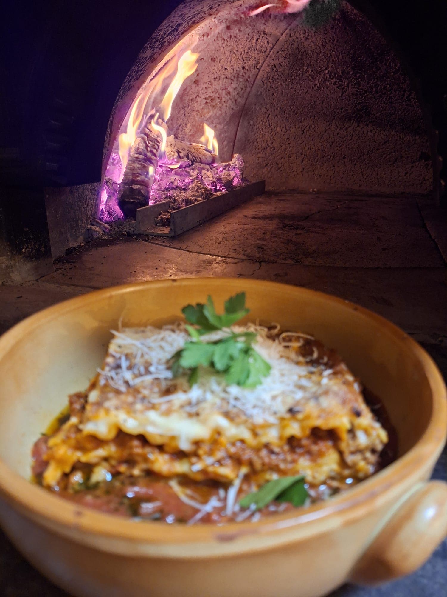 Lasagne in einem Keramiktopf vor dem Holzofen.